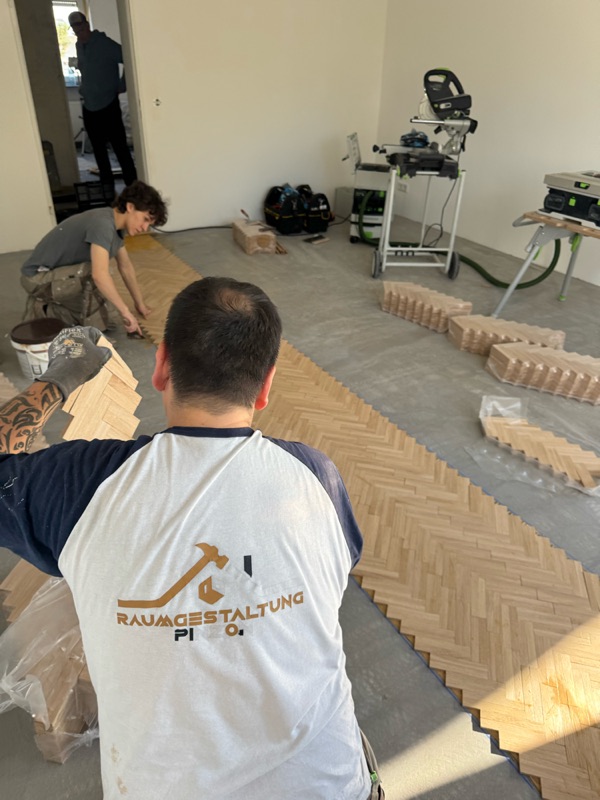 Zwei Handwerker verlegen Fischgrätparkett, Kappsäge und Werkzeug im Hintergrund