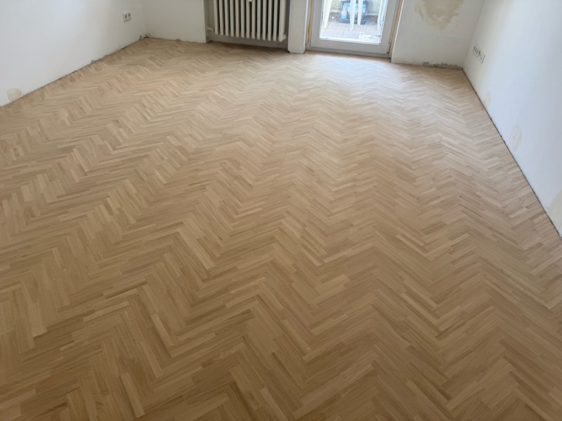 Hell geschliffenes Fischgrätparkett aus Eiche im leeren Zimmer mit Balkontür