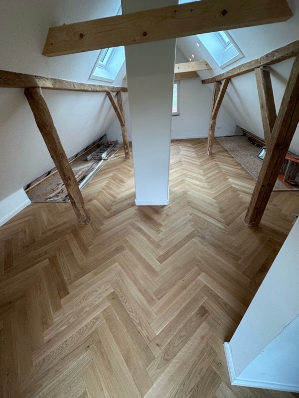 Dachgeschoss mit verlegtem Fischgrätparkett und sichtbaren Holzbalken