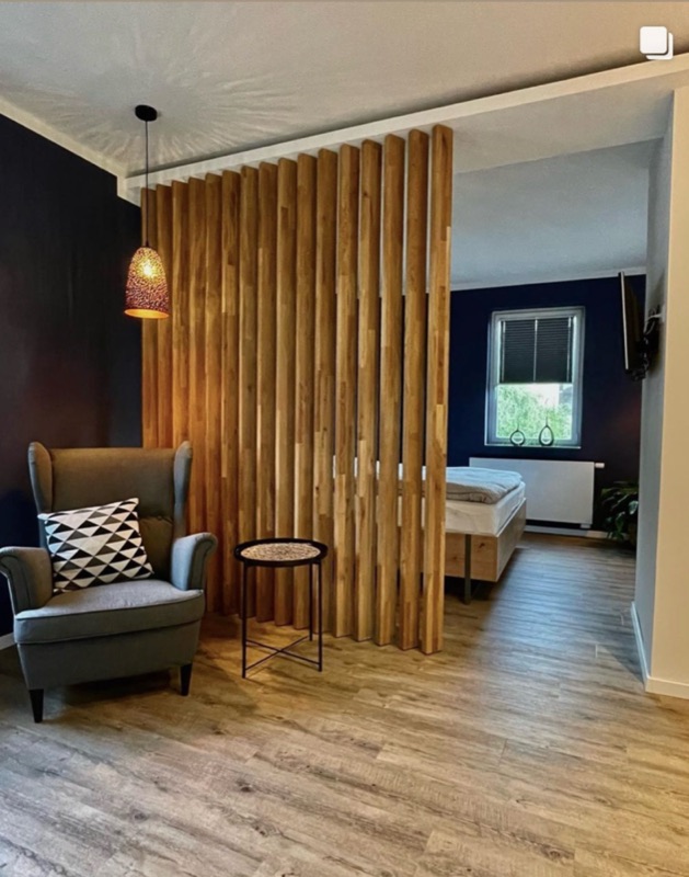 Raumteiler aus freistehenden Holzlamellen zwischen Sitzbereich und Schlafzimmer