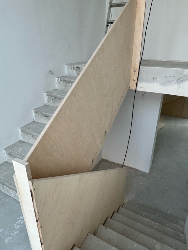 Brüstungskonstruktion aus Holzwerkstoffplatten an der rohen Betontreppe