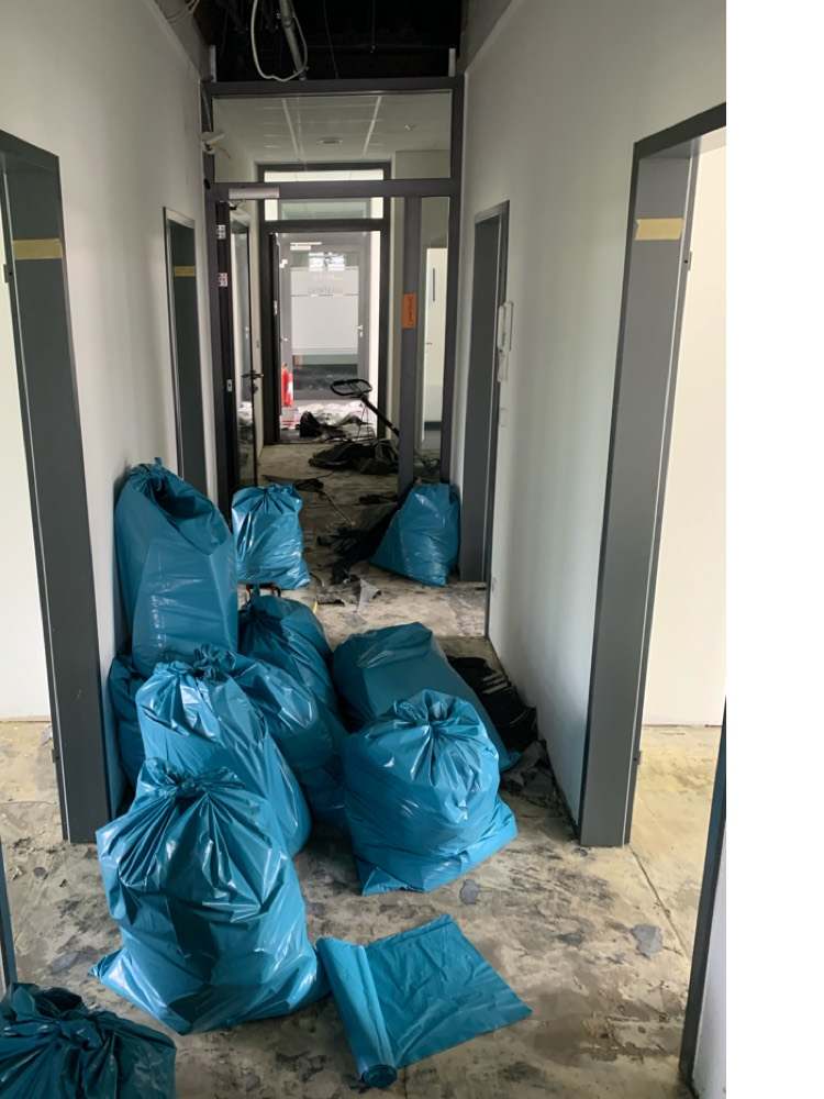 Entkernter Praxisflur mit Schuttsäcken und entferntem Bodenbelag